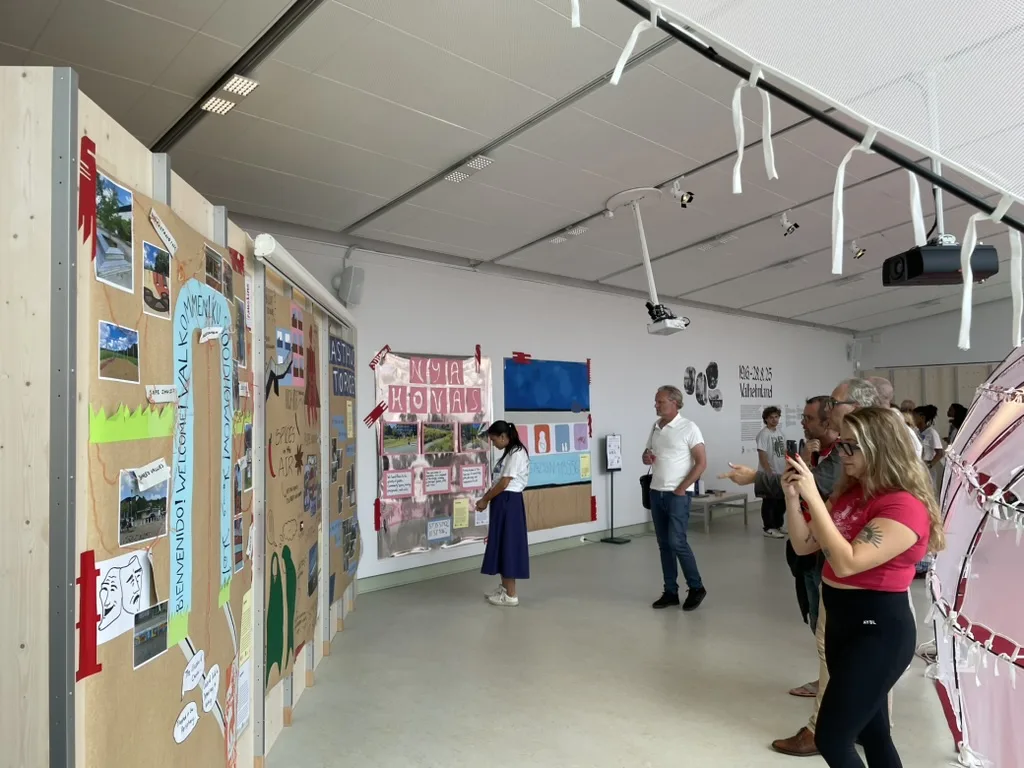 Visitants observant murals col·lectius fets amb retalls, fotografies i textos en una sala d’exposició.
