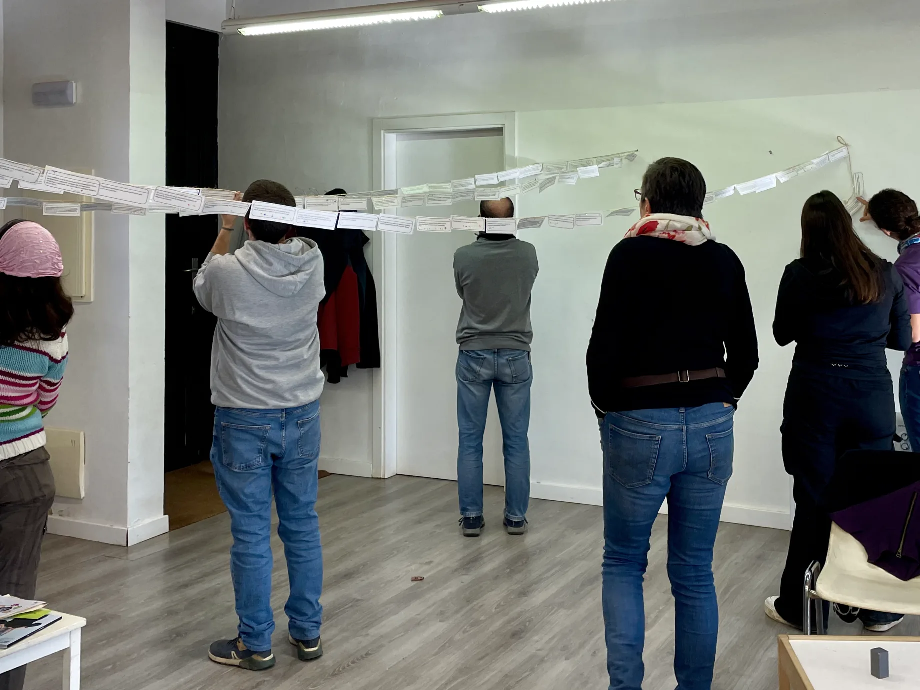 Participants d’un taller, d’esquena, pengen fileres de targetes de paper en cordills que travessen la sala.